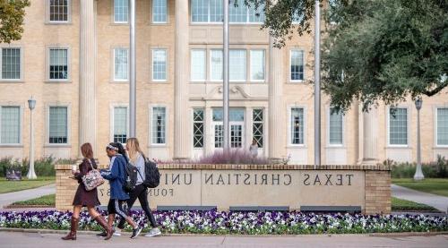 三个学生走在德州基督教大学的招牌前
